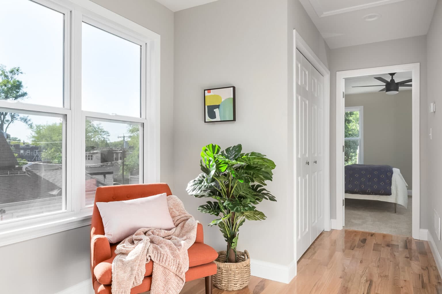 A hallway features a large window and a sitting area with an orange chair.