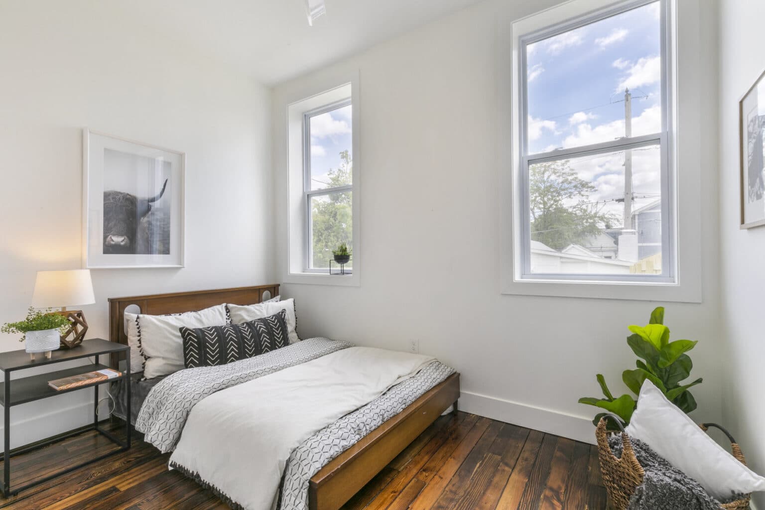 A bedroom with hardwood floor, platform bed, and two large windows.