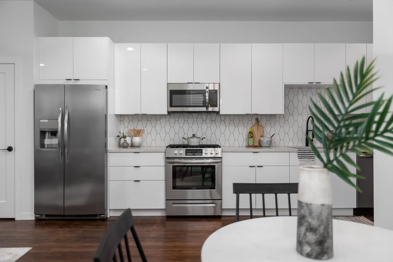A kitchen with hardwood floors, stainless steel appliance, and white cabinets with a plant in the foreground.