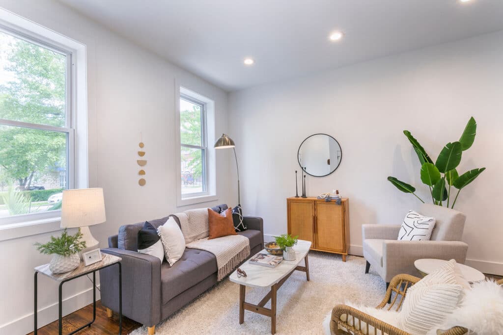 A living area with two large windows, couch, chairs, and decorations.