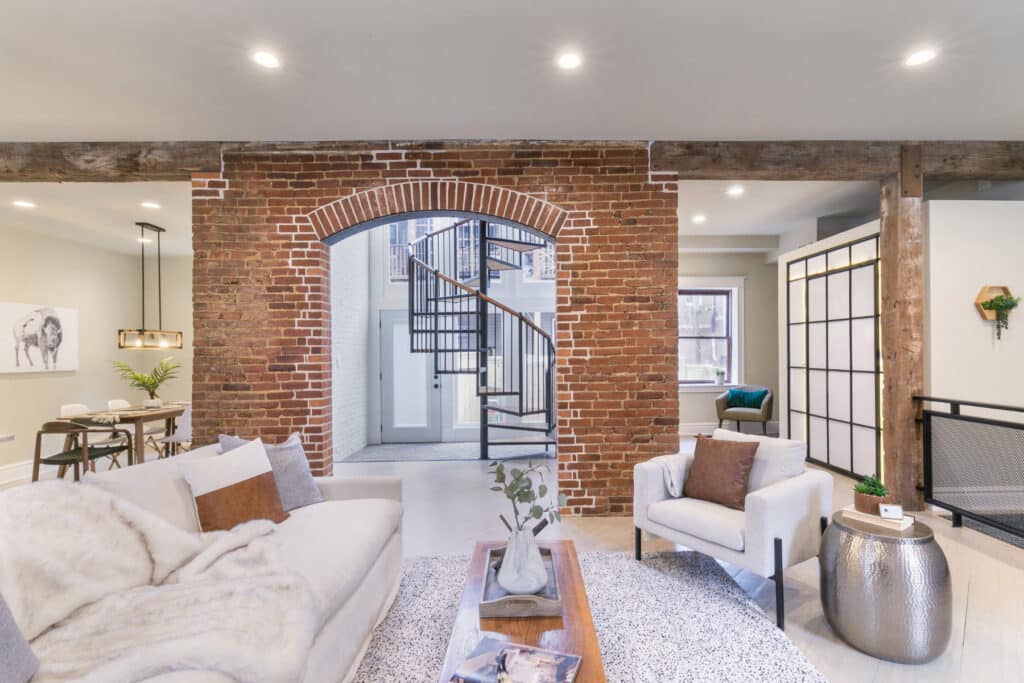 Living room with couch, coffee table, and chair has a backdrop of a brick wall.