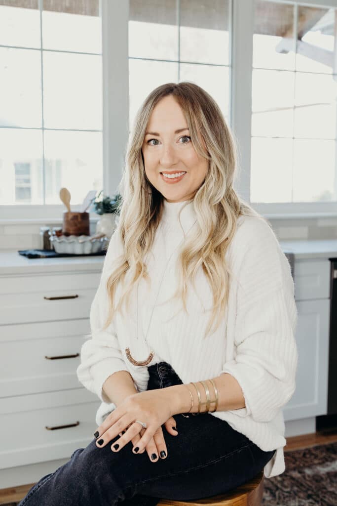 A woman wearing white poses for a portrait in a room with white walls and cabinets.
